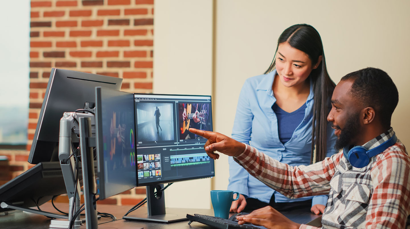 Marketing professional working at a standing desk in a modern office, shown from back or profile view, focused on a computer screen displaying a video creation interface